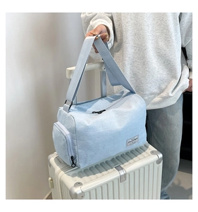 Detail view of light blue canvas bag featuring wide shoulder straps on a suitcase