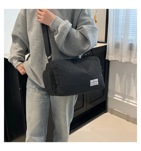 Detail of black canvas cylinder crossbody bag featuring white label and adjustable strap