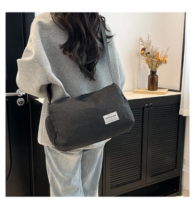 Detailed back view of a black canvas cylinder crossbody bag worn by a model