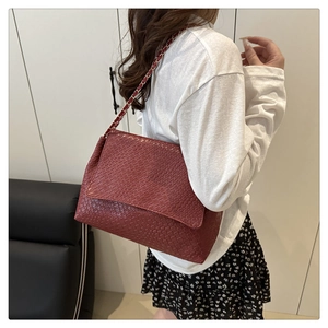 Détail du sac bandoulière bordeaux tressé avec chaîne dorée porté par un mannequin