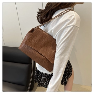 Detail of woven leather crossbody bag in dark brown with metal chain strap on model