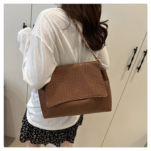 Gros plan sur la texture tressée marron foncé et la bandoulière chaîne de ce sac