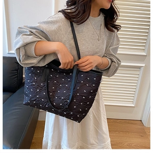 Close-up of black quilted tote bag with white bow embroidery and slim shoulder straps