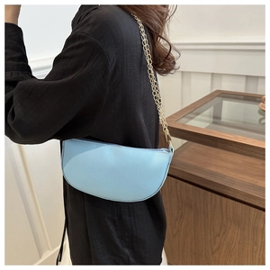 Detail of light blue crescent leather shoulder bag with gold chain strap on model