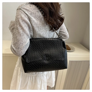 Lifestyle shot of black woven leather shoulder bag with gold chain strap on model