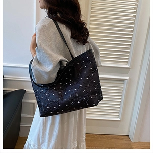 Detail of black tote bag featuring white bow patterns and pleated texture on model