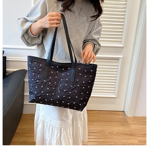 Quilted tote bag with white bow prints shown on shoulder in cozy indoor setting