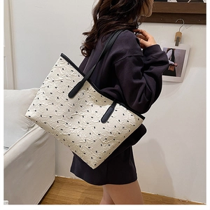 Detail of off-white tote bag with pleated texture and black bow patterns on shoulder