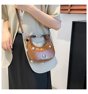Detail of a brown crescent leather bag with silver studs and a slim shoulder strap