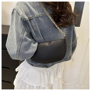 Detail view of a black semi-circular crossbody bag with litchi texture and gold chain strap