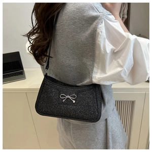 Close-up of black sequined shoulder bag with a silver metal bow on a female model