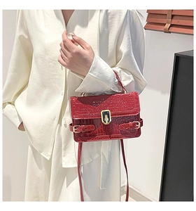 Close-up of bright red crocodile-embossed leather handbag with gold metal lock and strap