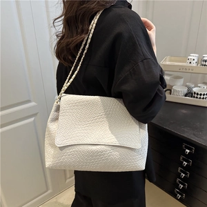 White woven leather shoulder bag with gold chain strap shown on model in home setting