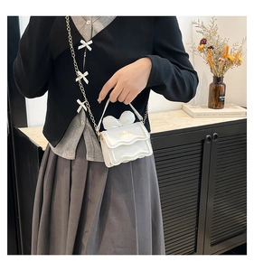 Détail du mini sac blanc en cuir PU avec nœud 3D, rabat ondulé et bandoulière chaîne dorée