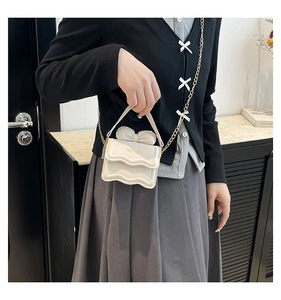 Détail du sac sous le bras crème avec nœud et bandoulière en chaîne dorée porté par un mannequin