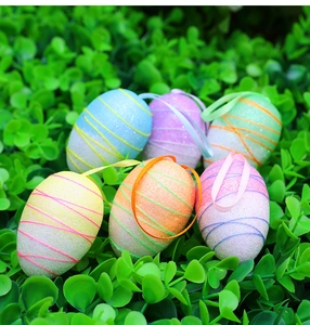 Glittery colorful Easter eggs with ribbons hanging over green leaves for festive decoration