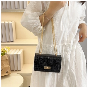 Detail of black crocodile texture shoulder bag with gold chain strap and twist lock