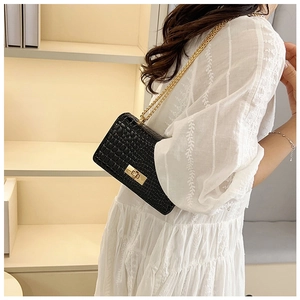 Detail of black patent faux crocodile leather bag with gold clasp and chain on lace dress