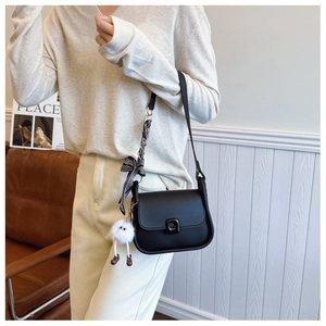Detail of black crossbody bag with decorative striped ribbon and white plush monster charm