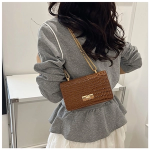 Close-up of brown crocodile texture handbag with gold chain strap on a model