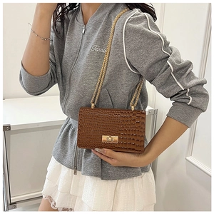 Detailed view of brown crocodile texture flap bag with gold chain strap and metal twist lock
