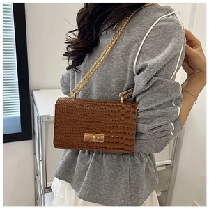 Detail of crocodile embossed leather and golden clasp on brown crossbody bag