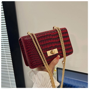 Detail of red crocodile textured faux leather bag with gold chain strap and turn lock