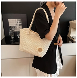 Detail of a beige woven straw tote bag featuring a sunflower ornament and rope handle
