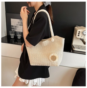 Detail of a beige straw tote bag with a large sunflower and cotton rope handles