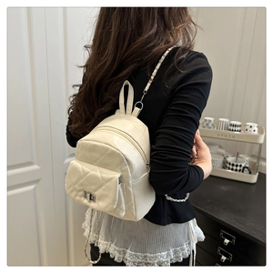 Detail of cream quilted mini backpack with gold chain strap worn by a model