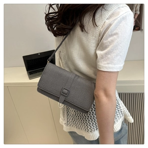 Sac bandoulière chic en tissu gris porté par un mannequin dans un bureau moderne