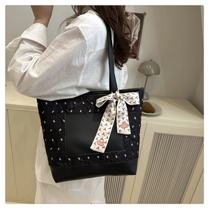 Quilted black tote bag with silk scarf detail worn by model in a minimalist room