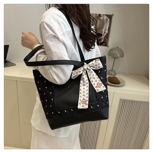 Detail of black quilted tote bag with white patterns and decorative silk scarf on strap