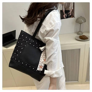 Detail of a black patterned tote bag featuring a bow print and decorative silk scarf strap