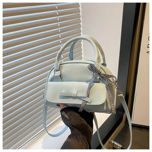 Close-up of light blue handbag featuring a bow detail and a checkered ribbon on the handle