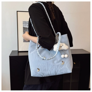 Dettaglio borsa tote azzurra con farfalla dorata e tracolla intrecciata elegante