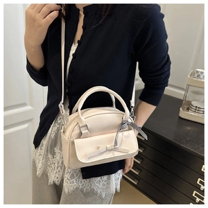 Close-up of cream square handbag with bow accent and plaid ribbon detail on shoulder