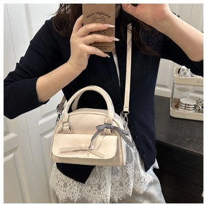 Detail of cream PU leather handbag with decorative bow and black-white checkered silk ribbon