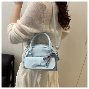 Light blue bow Boston bag shown on model with white outfit in minimalist indoor setting
