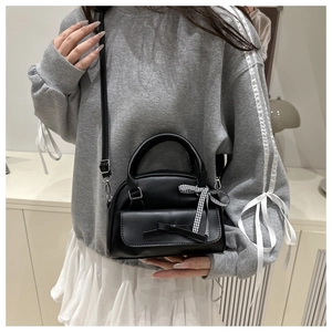 Model showcasing a black crossbody bag with bow detail and checkered ribbon strap