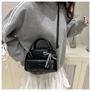 Detail of black leather shell bag with ribbon bow handle and plaid silk scarf