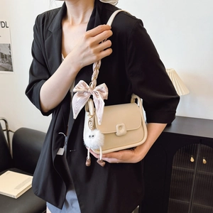 Sac bandoulière beige élégant avec nœud et breloque en peluche sur un mannequin
