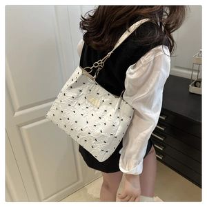 Détail du sac plissé blanc avec broderies de nœuds noirs et bandoulière dorée