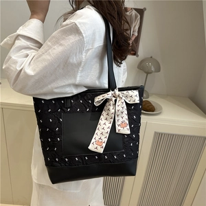 Quilted black tote bag with bow patterns and scarf handle in a bright interior setting