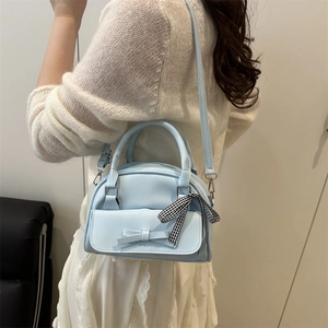 Light blue shell handbag with bow detail and plaid ribbon shown on a model