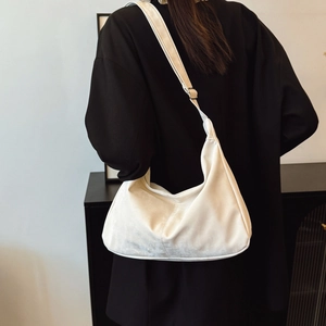 White nylon crescent tote bag shown on model with black blazer in a minimalist interior