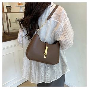 Deep brown leather crescent bag with gold metal clasp shown on a model in a cafe