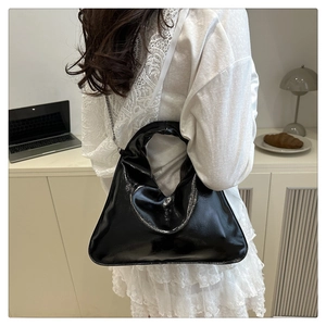 Detailed view of black heart-shaped chain bag with glossy finish on shoulder strap