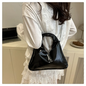 Detail of black glossy bucket bag with circular hollow handle and silver metal chain strap