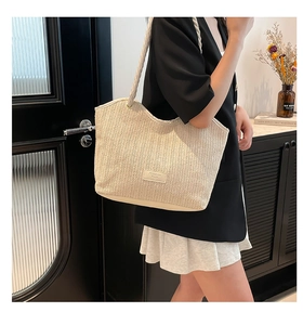 Close-up of beige woven straw tote bag with braided handles and fashion leather label